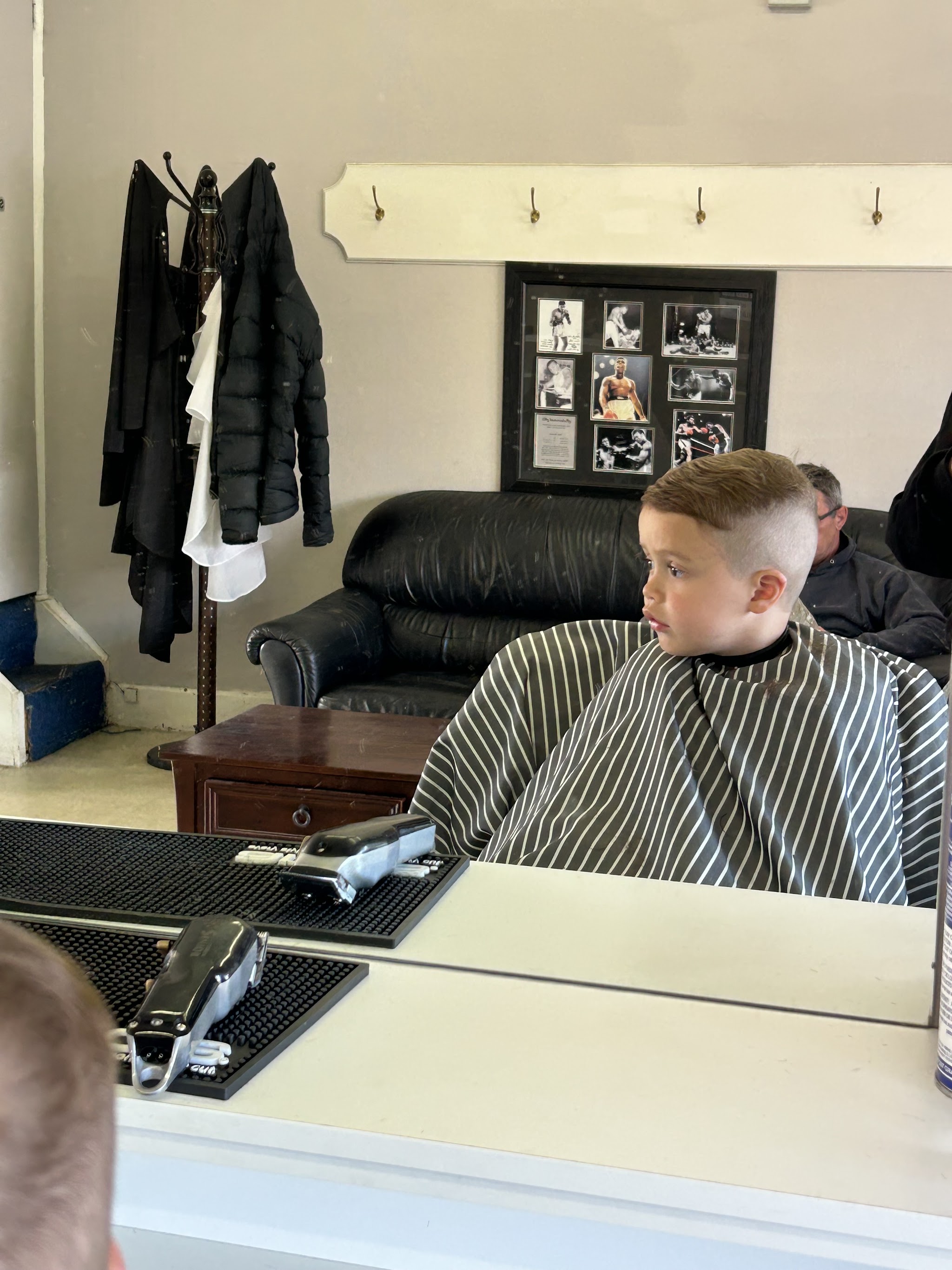A young customer with a fresh skin fade in the chair at Raymondo’s, framed Muhammad Ali photos on the wall behind